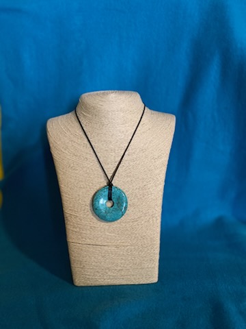 A round turquoise-colored stone pendant on a necklace display